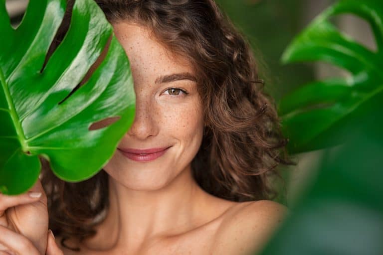 Beautiful woman with curly hair behind big green leaf