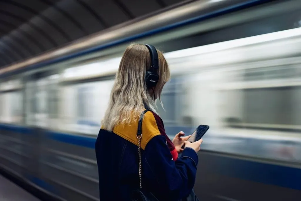 blonde girl with headphones looking at her smartphone, at the metro station