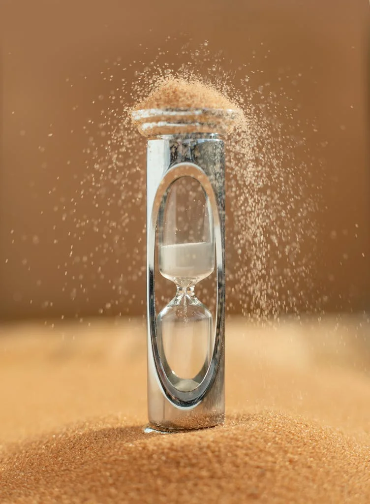 Close-up of an hourglass with sand falling, capturing the essence of time against a yellow background.