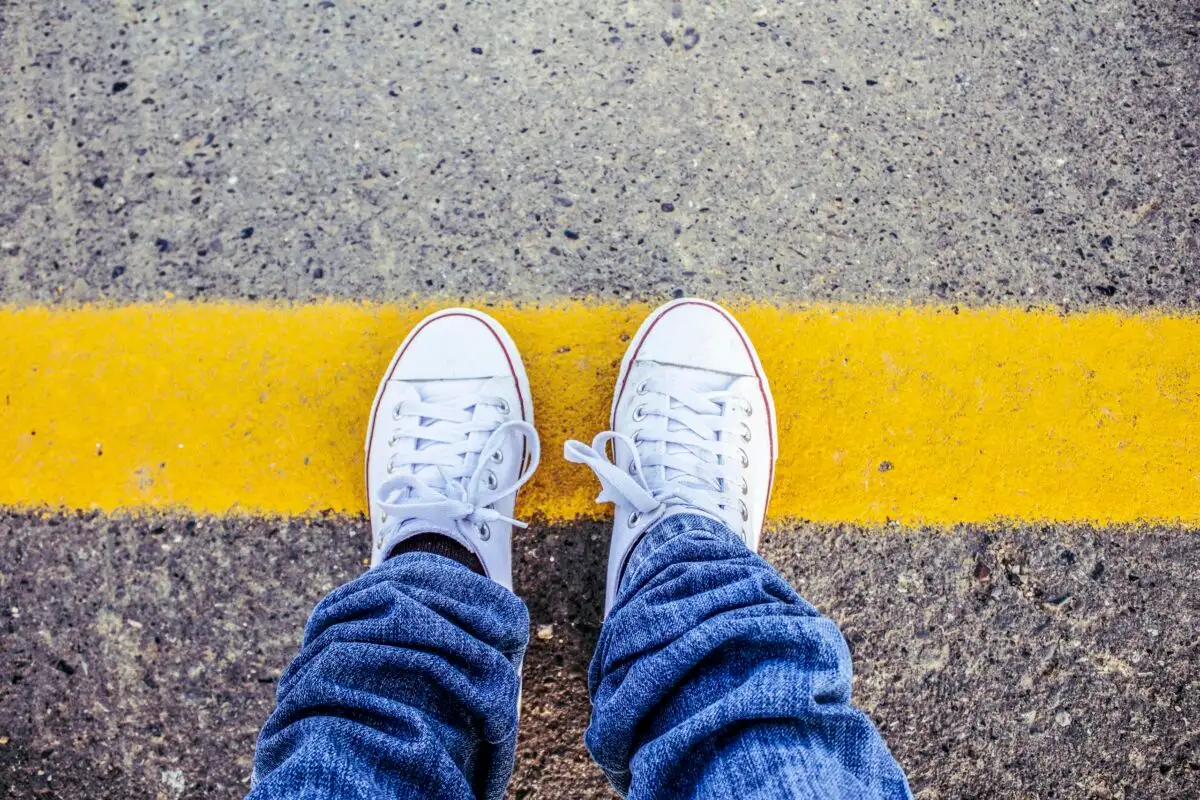 Close-up of white sneakers on pavement with a yellow line, symbolizing boundaries.