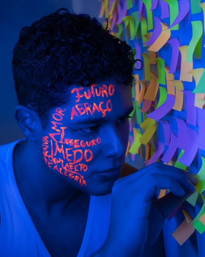 Man with neon face paint next to colorful sticky notes in blue light.