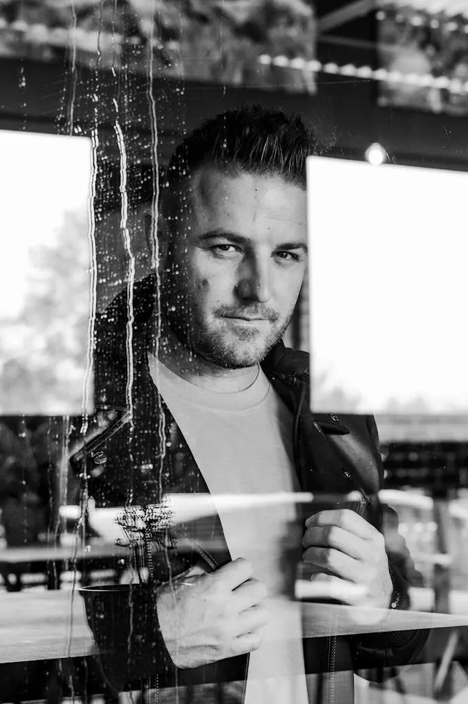 Man smiling behind a window, it's raining, black and white
