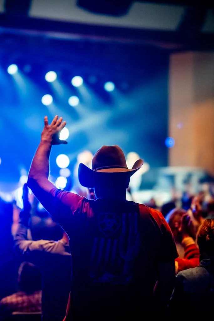 Energetic scene at a country music concert with a fan in a cowboy hat raising his hand.