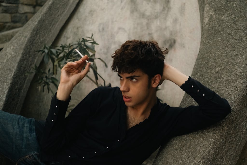 Stylish young man in black shirt relaxing outdoors in İstanbul, capturing a moody urban moment.