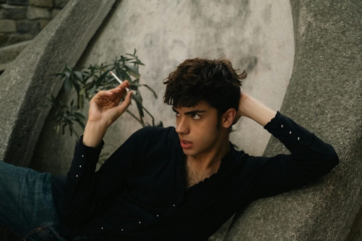 Stylish young man in black shirt relaxing outdoors in İstanbul, capturing a moody urban moment.