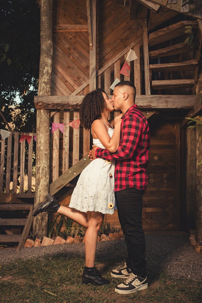 A couple shares a romantic kiss outside a rustic cabin with festive decorations.