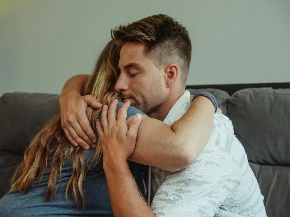 A heartfelt embrace between two adults on a sofa, expressing love and affection.
