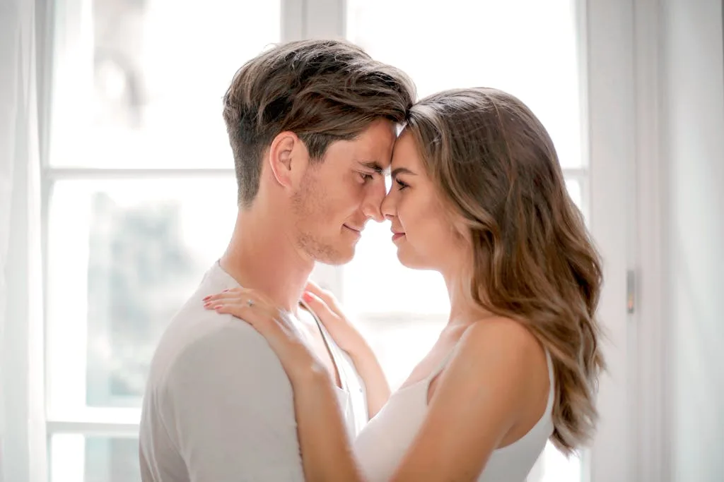 A loving couple shares a tender moment by a sunlit window, capturing romance.