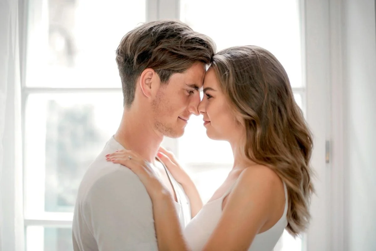 A loving couple shares a tender moment by a sunlit window, capturing romance.