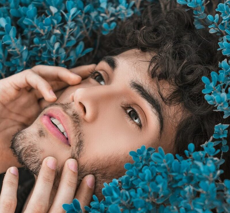 Close-up portrait of a man surrounded by vibrant blue flowers, expressing a serene mood.