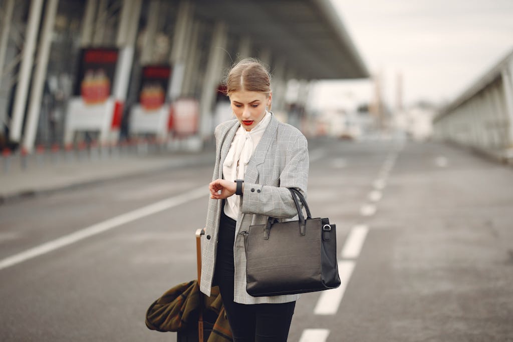 A businesswoman checks her watch while waiting at an airport terminal, looking concerned.