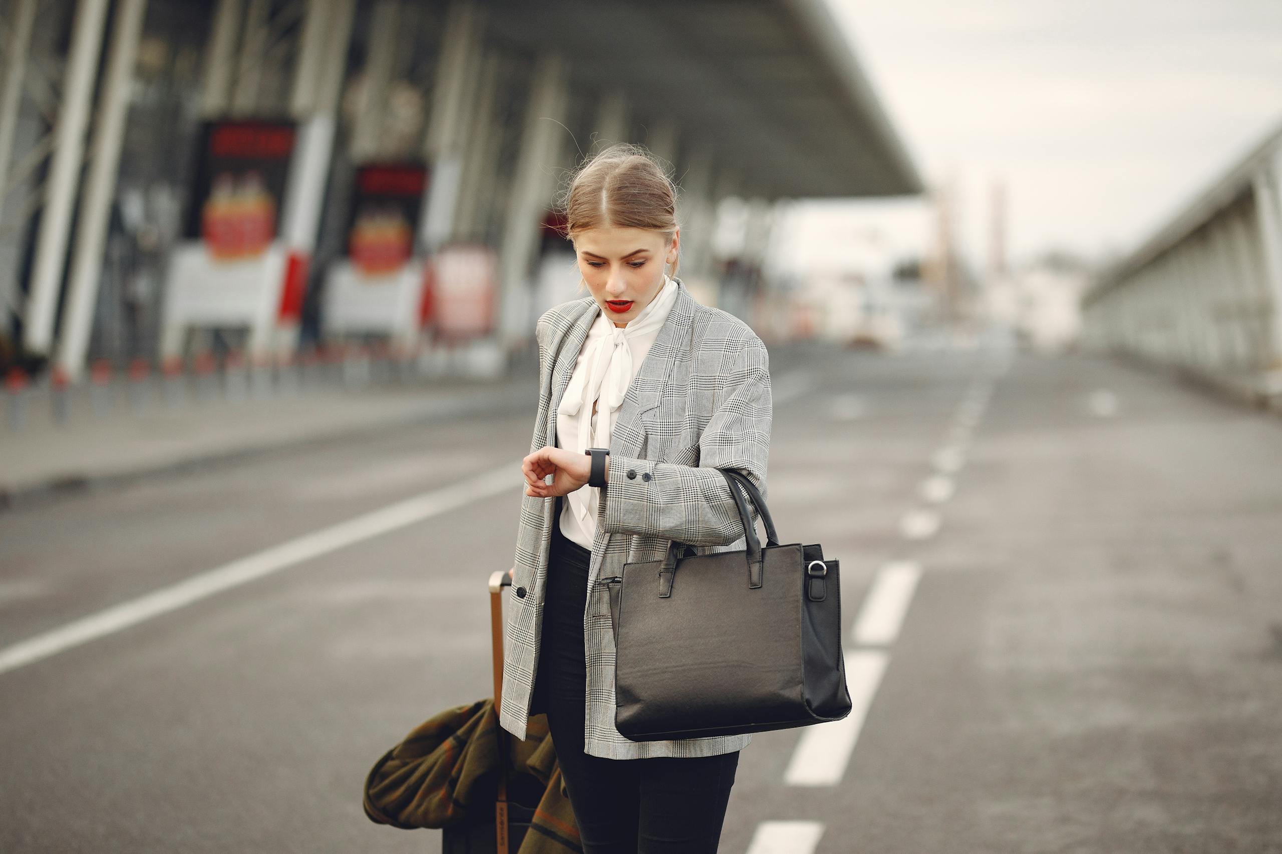 A businesswoman checks her watch while waiting at an airport terminal, looking concerned.