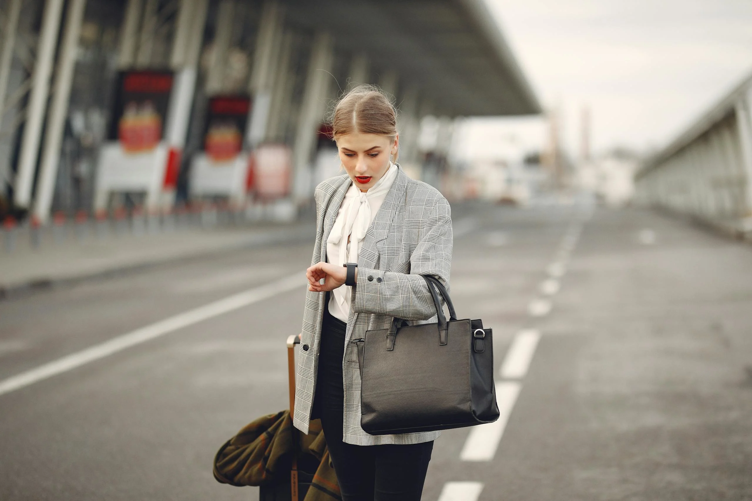 A businesswoman checks her watch while waiting at an airport terminal, looking concerned.