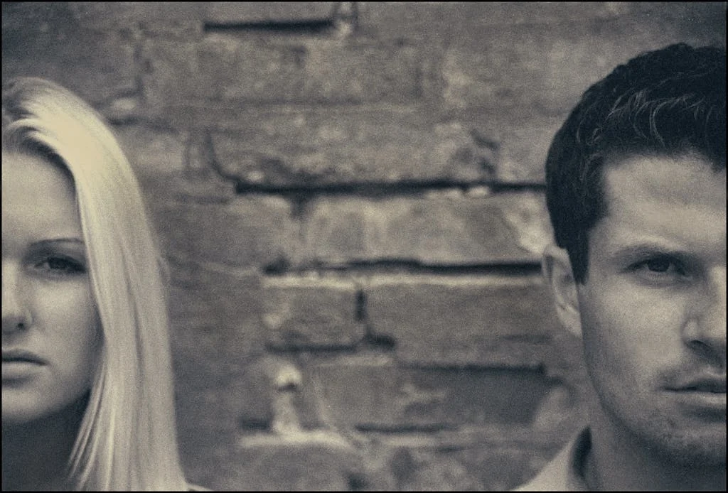 Close-up artistic portrait of a couple posing against a brick wall, highlighting their facial expressions.