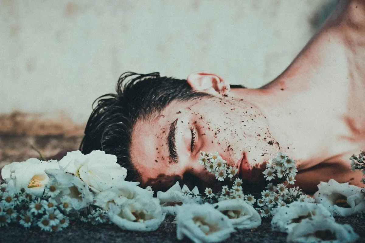 A contemplative image of a man lying among white flowers, conveying introspection.