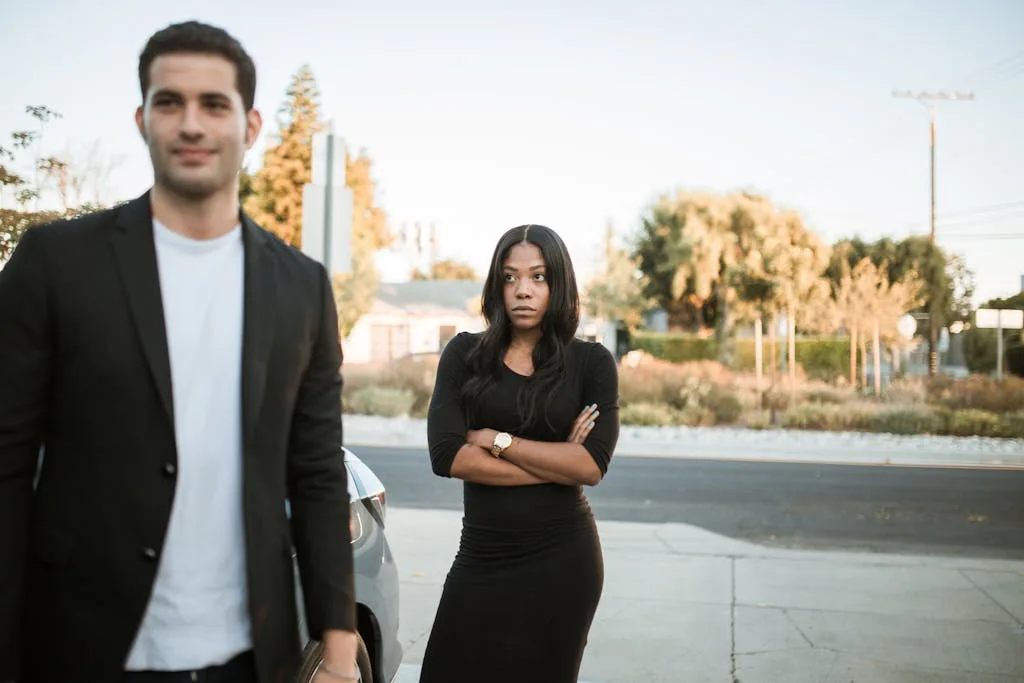 A couple facing relationship tension outdoors with arms folded, expressing emotions.