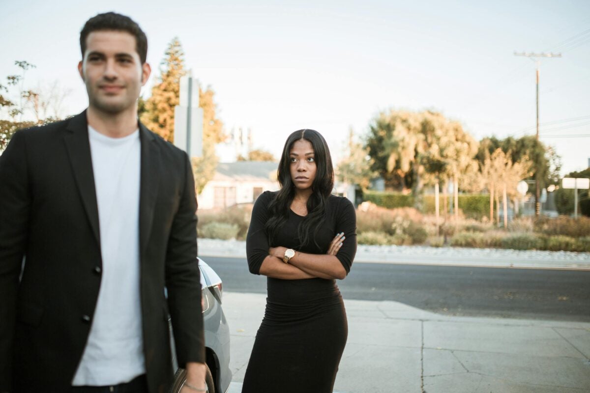 A couple facing relationship tension outdoors with arms folded, expressing emotions.