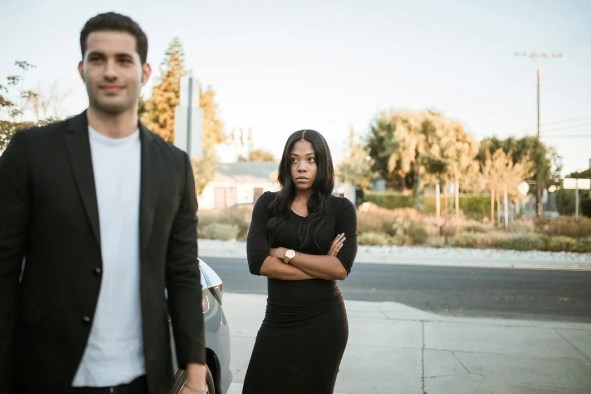 A couple facing relationship tension outdoors with arms folded, expressing emotions.