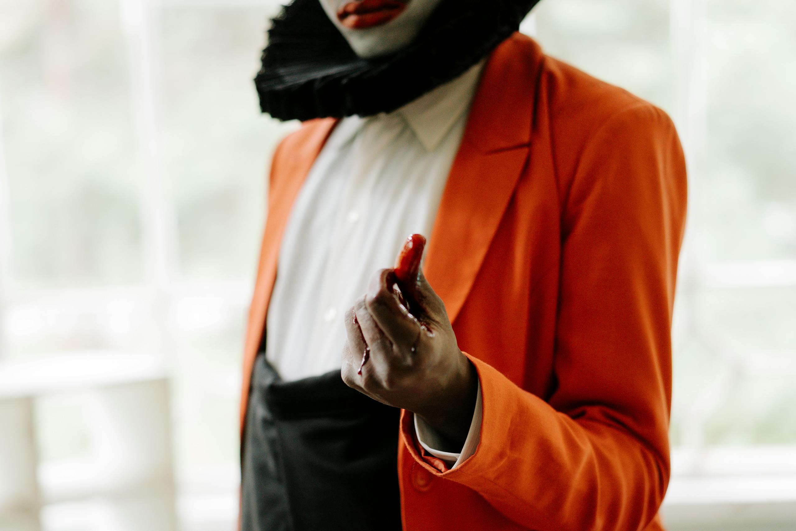A spooky close-up of a clown in an orange jacket with a bloody hand, perfect for Halloween.