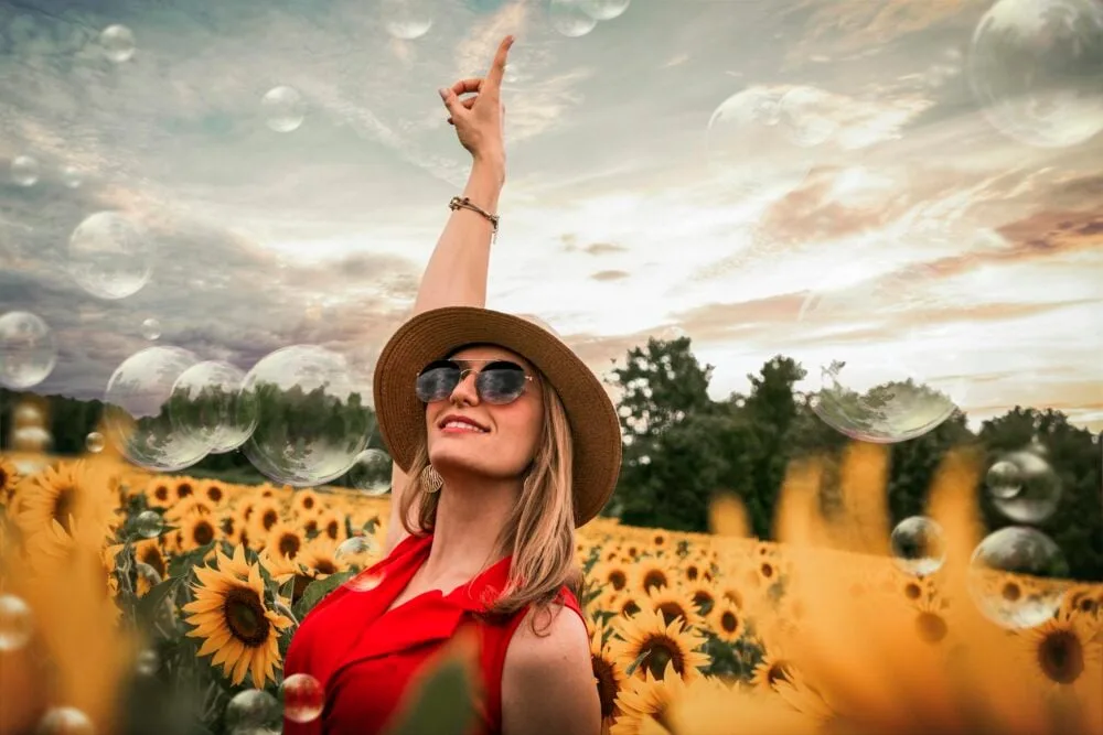 Cheerful woman enjoying a sunny day in a vibrant sunflower field while bubbles float around.