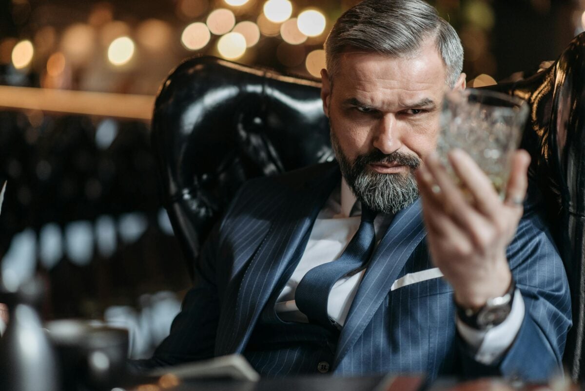 Mature businessman in a suit inspecting a glass of whiskey with focus indoors.