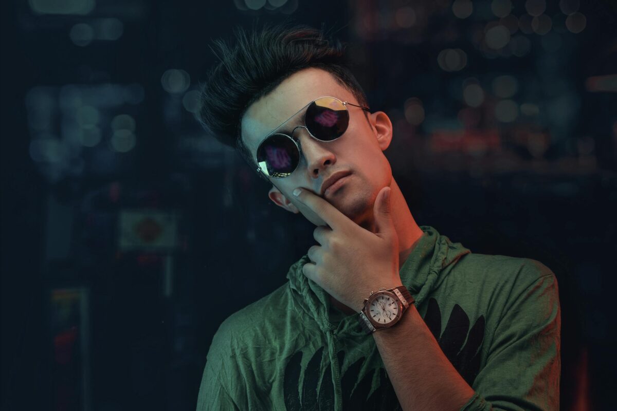 Portrait of a young man in sunglasses and neon lighting, showcasing modern fashion.