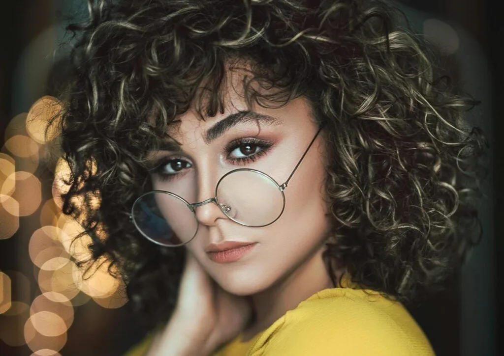 Stylish portrait of a woman with curly hair and eyeglasses in a vibrant setting.