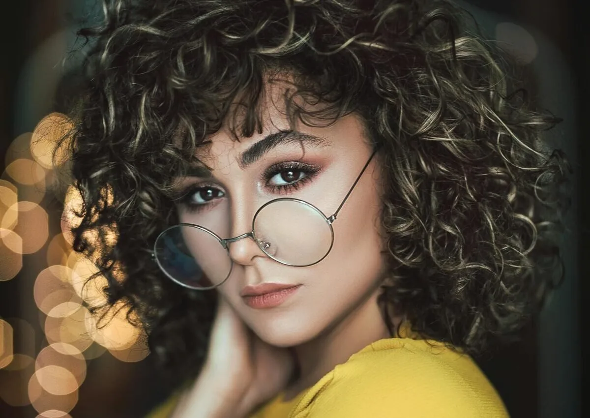 Stylish portrait of a woman with curly hair and eyeglasses in a vibrant setting.