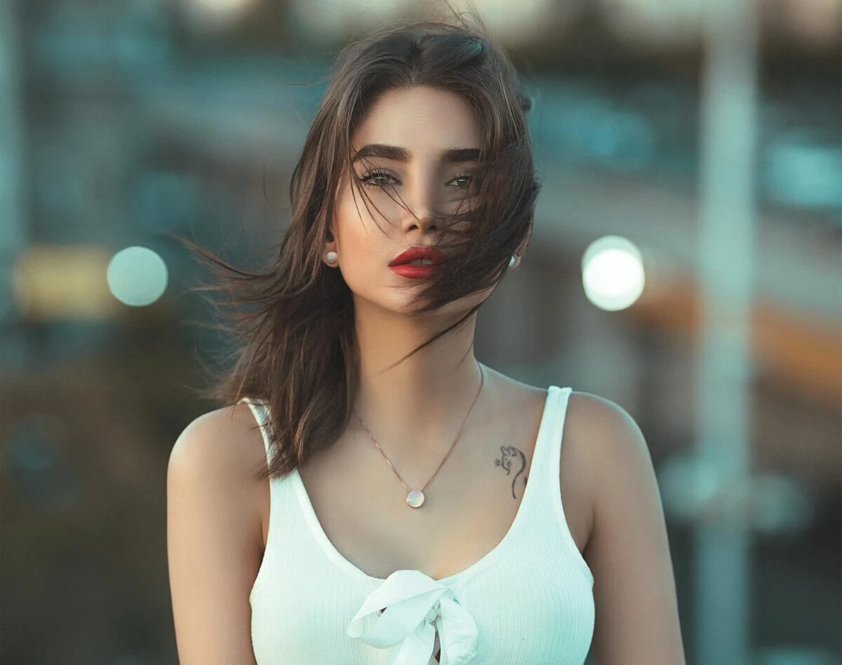 Stylish woman in white top posing outdoors with urban backdrop.