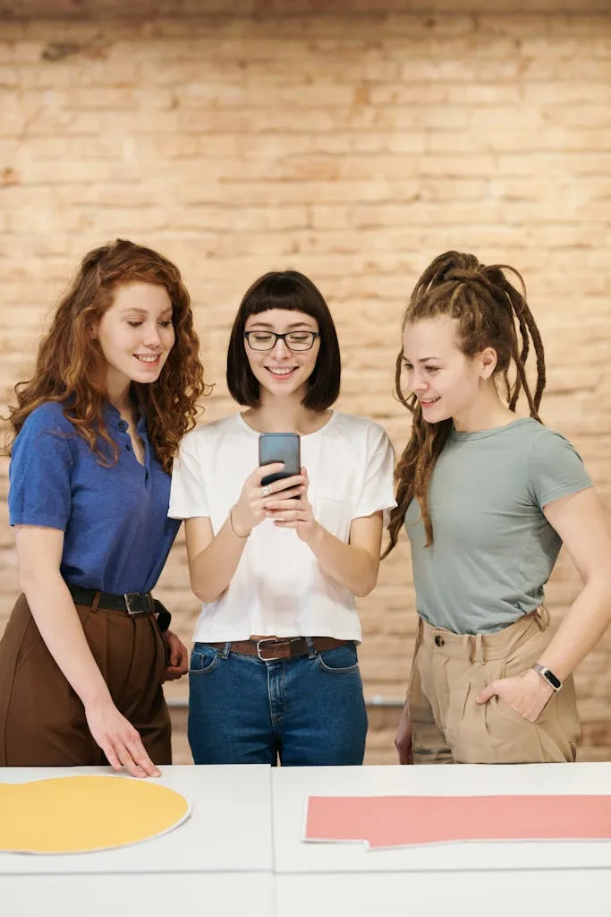 Three young women with stylish looks sharing a happy moment over a smartphone indoors.