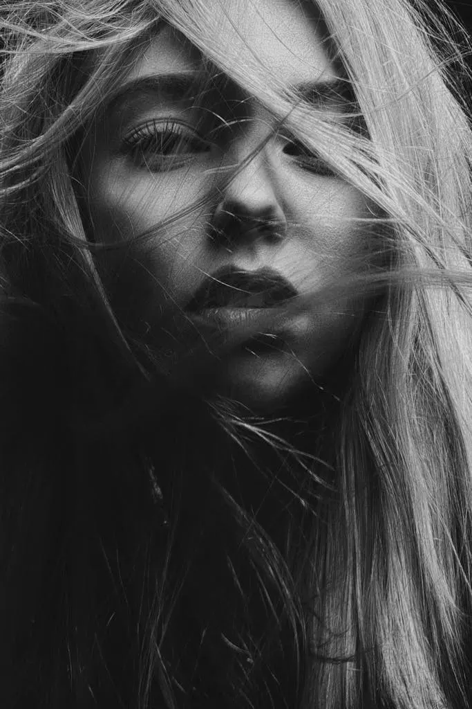A dramatic black and white portrait capturing a woman's face with flowing hair. High contrast mood.