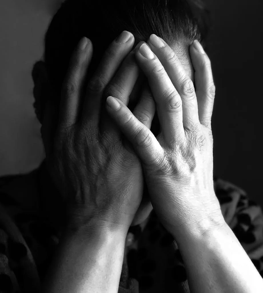 Black and white close-up portrait showing a woman covering her face in a moment of emotion.
