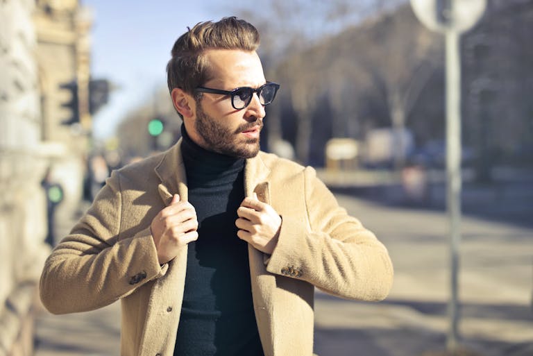 Fashionable young man with sunglasses poses outdoors in a sunny Budapest street scene.