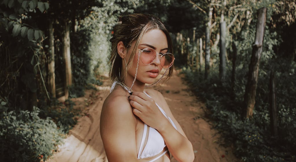 Portrait of a stylish woman in a forest pathway wearing sunglasses and summer attire.
