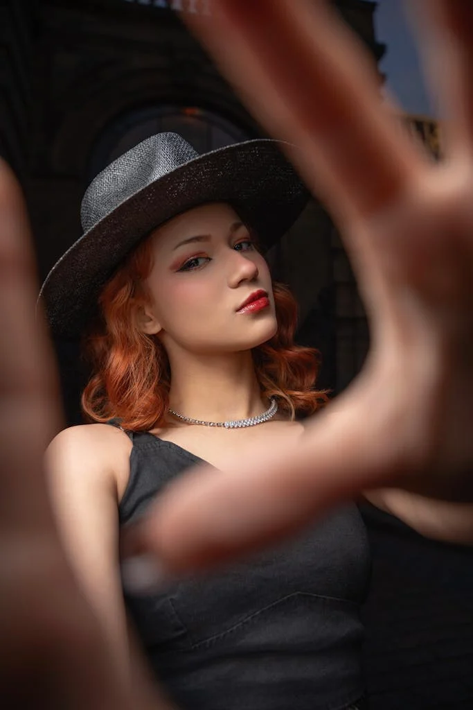 Stylish adult woman with red hair wearing a wide-brim hat, posing confidently outdoors at night.