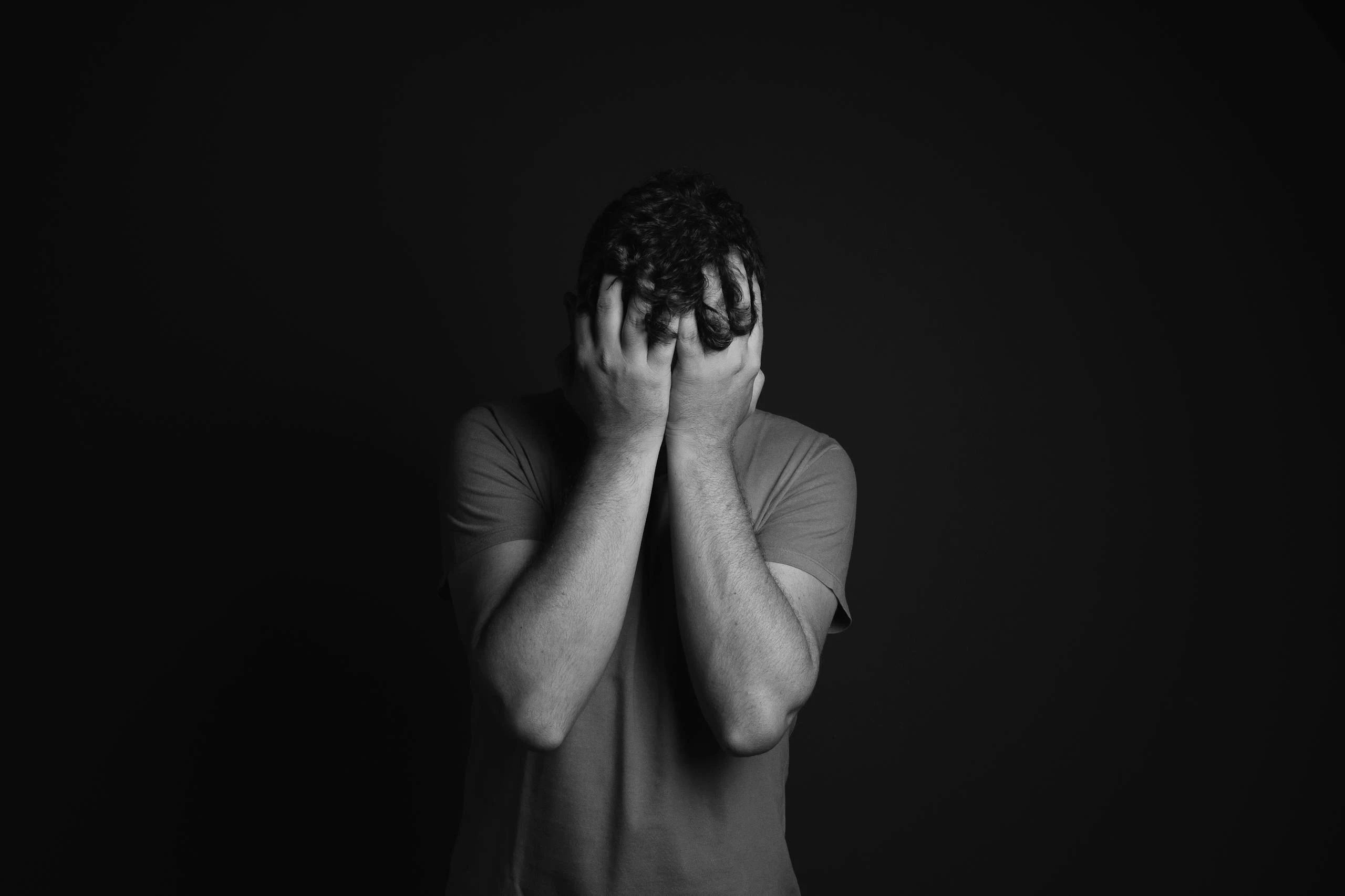 A grayscale portrait of a man covering his face, depicting emotion and mental health themes.