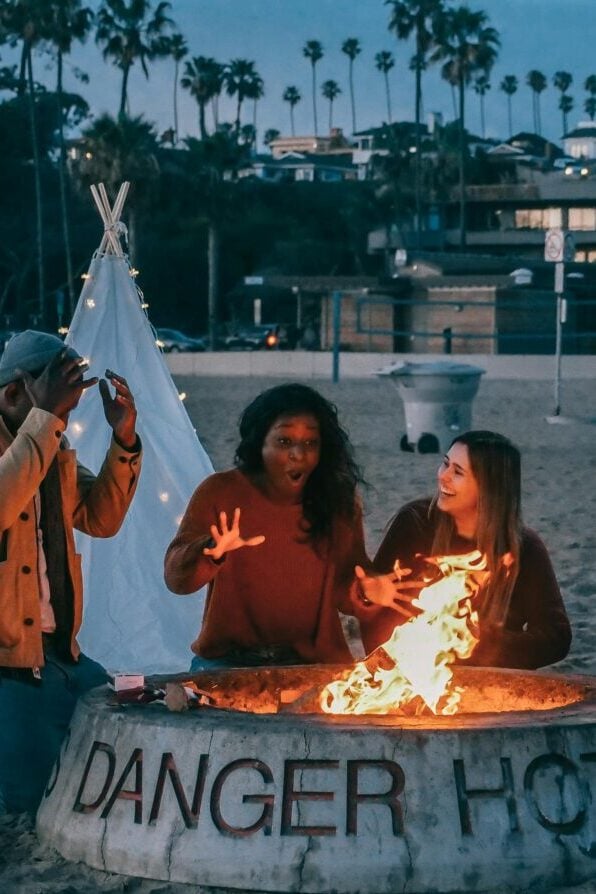 A diverse group of friends enjoying a bonfire on the beach at sunset, highlighting fun and togetherness.