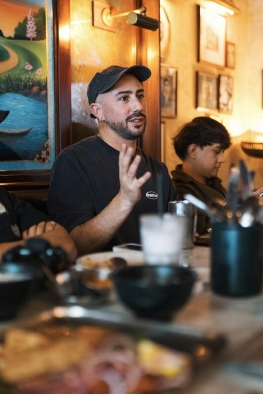 A group of adults in casual conversation at a restaurant with food and drinks on the table.