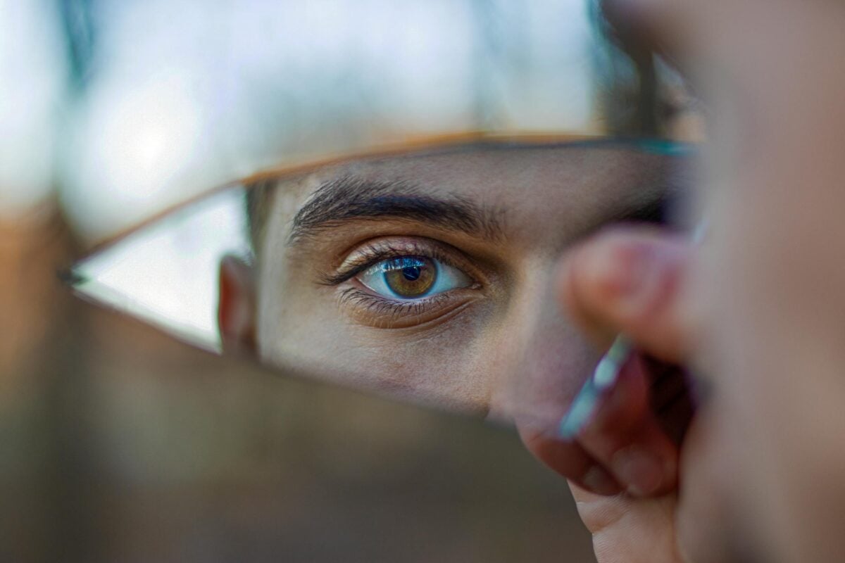 A striking portrait reflecting a blue eye in a piece of broken mirror outdoors.