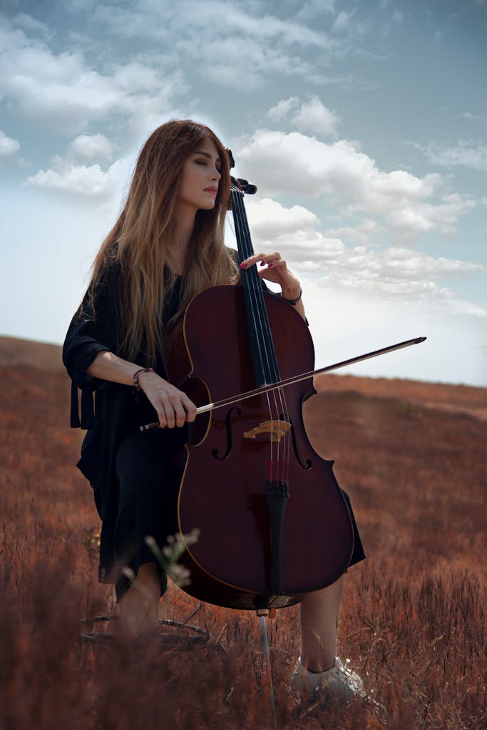 A young woman plays the cello in a serene outdoor setting under a bright sky.