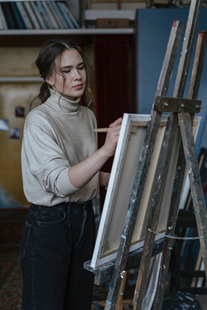 Caucasian woman artist painting on canvas in an indoor art studio setting.