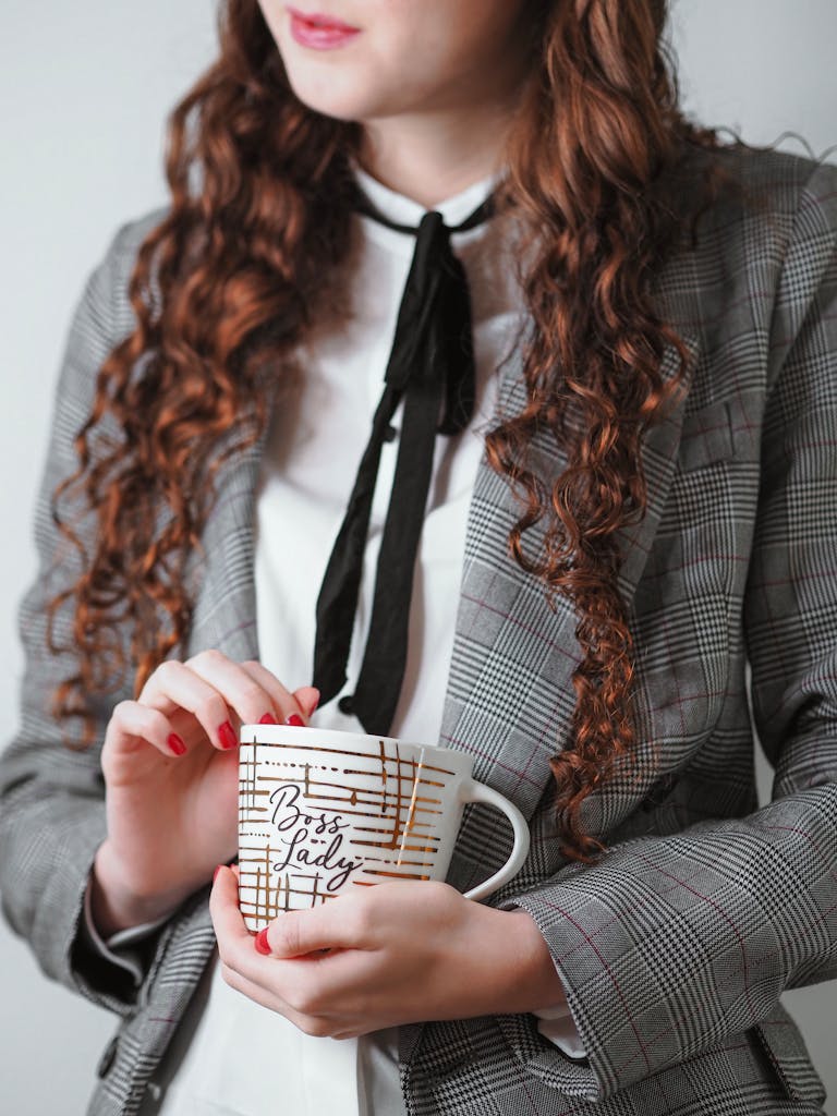 Close-up of a woman holding a 'Boss Lady' mug, dressed in a stylish gray suit.