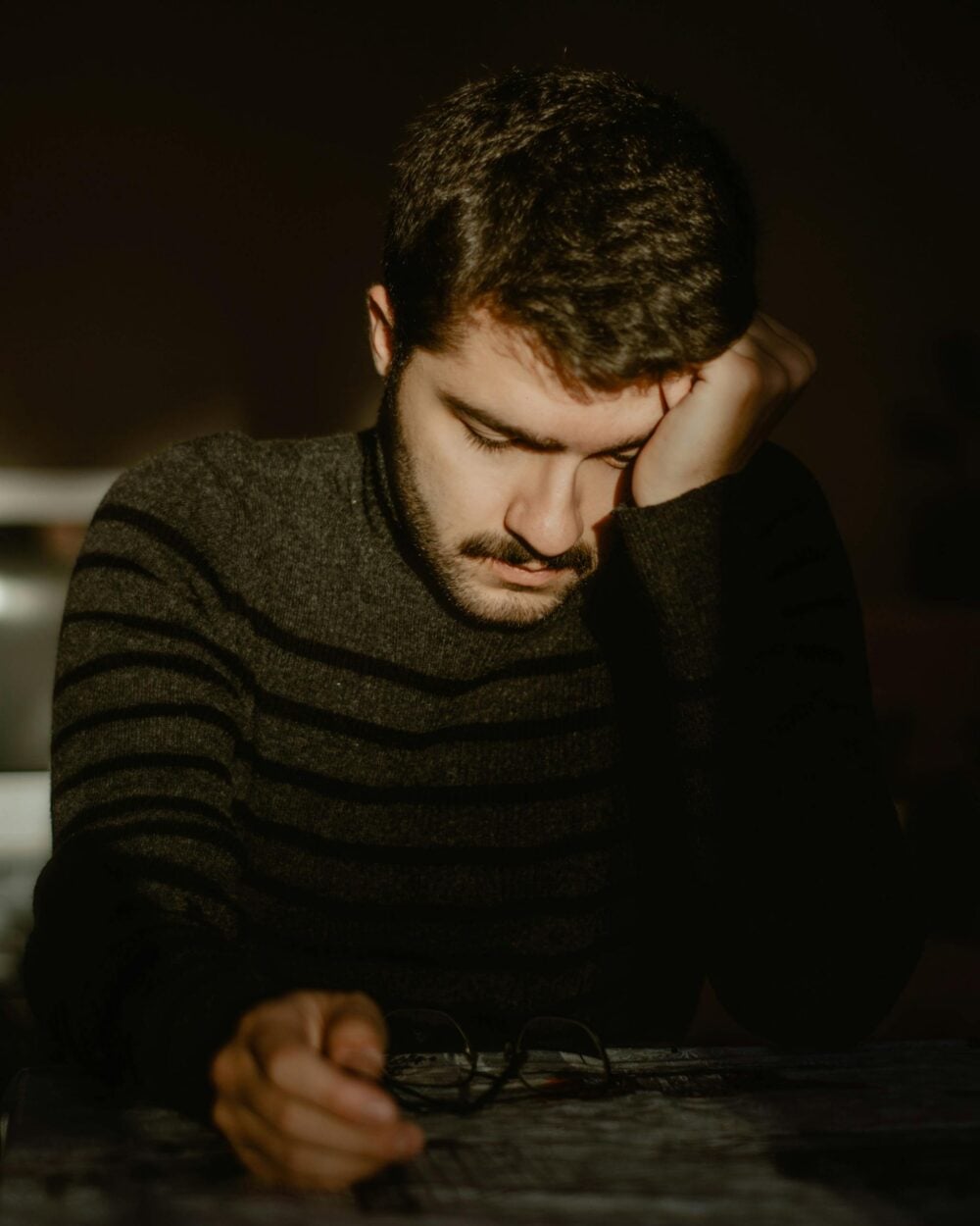 Portrait of a young man sitting alone indoors, reflecting in a dimly lit room.