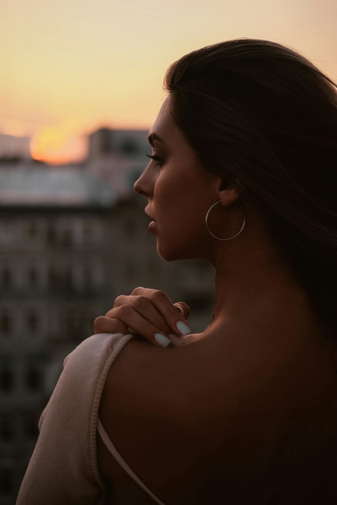 Profile of a woman gazing at the sunset from a cityscape view, exuding elegance and calmness.