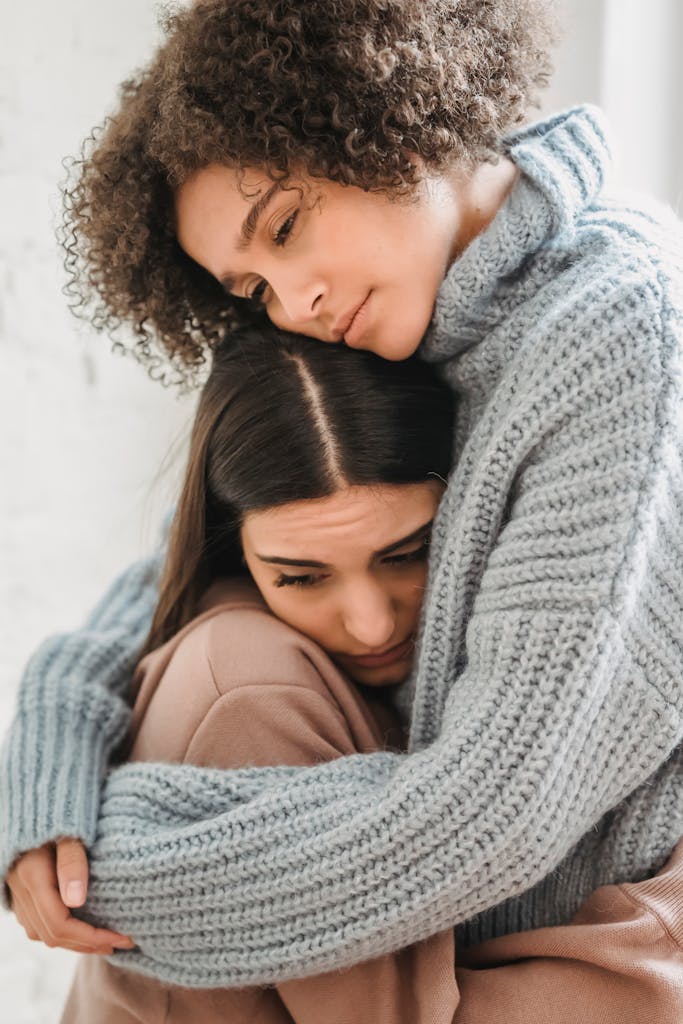 Two women comforting each other with a warm embrace inside a room.