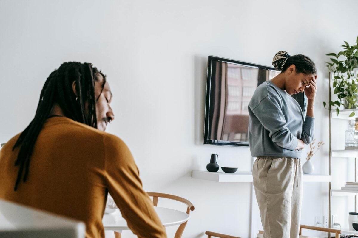 Young black female standing near table while arguing with male while sitting in light room
