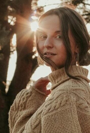Young woman in cozy sweater standing outdoors with sun flare. Tranquil fall setting in Minsk.