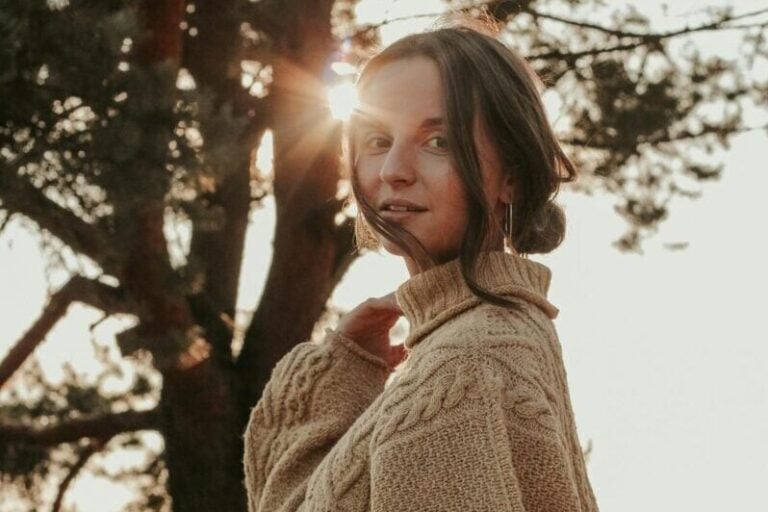Young woman in cozy sweater standing outdoors with sun flare. Tranquil fall setting in Minsk.