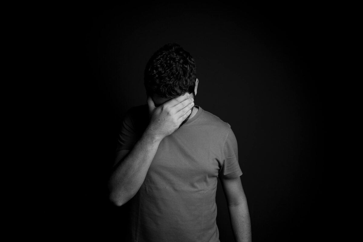 A black and white portrait of a man hiding his face, conveying deep emotion and introspection.