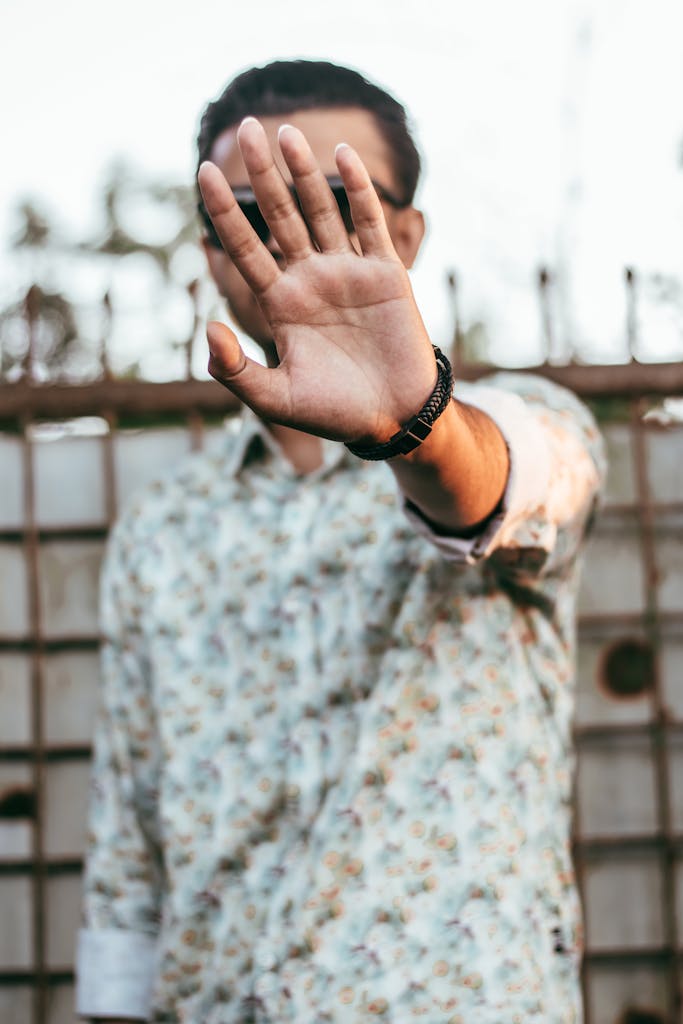 A man in a floral shirt holds his hand in front, creating a stopping gesture.